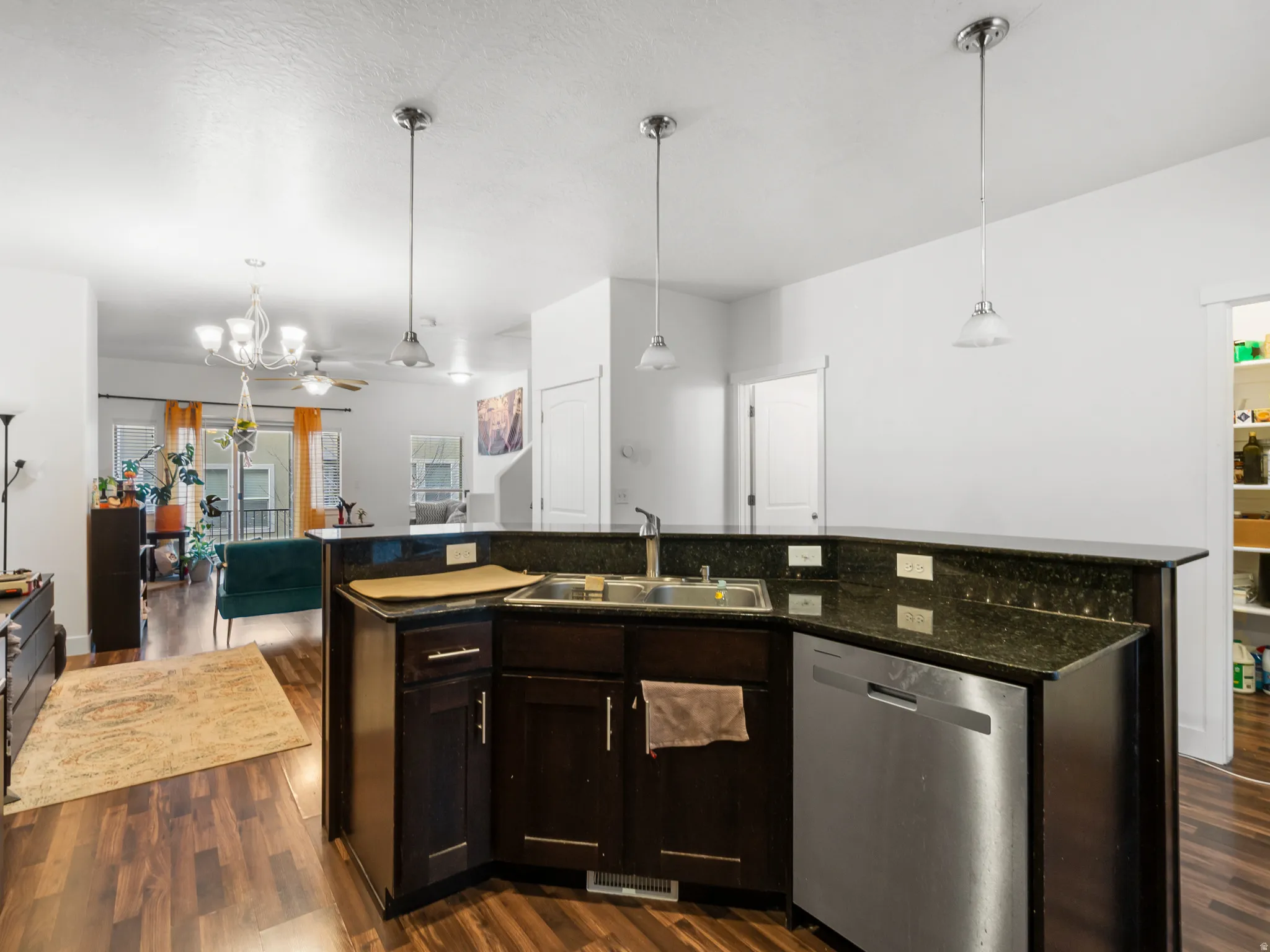 Kitchen featuring open floor plan, dark wood finish cabinets, a center island with sink, dishwasher, and dark wood-style flooring