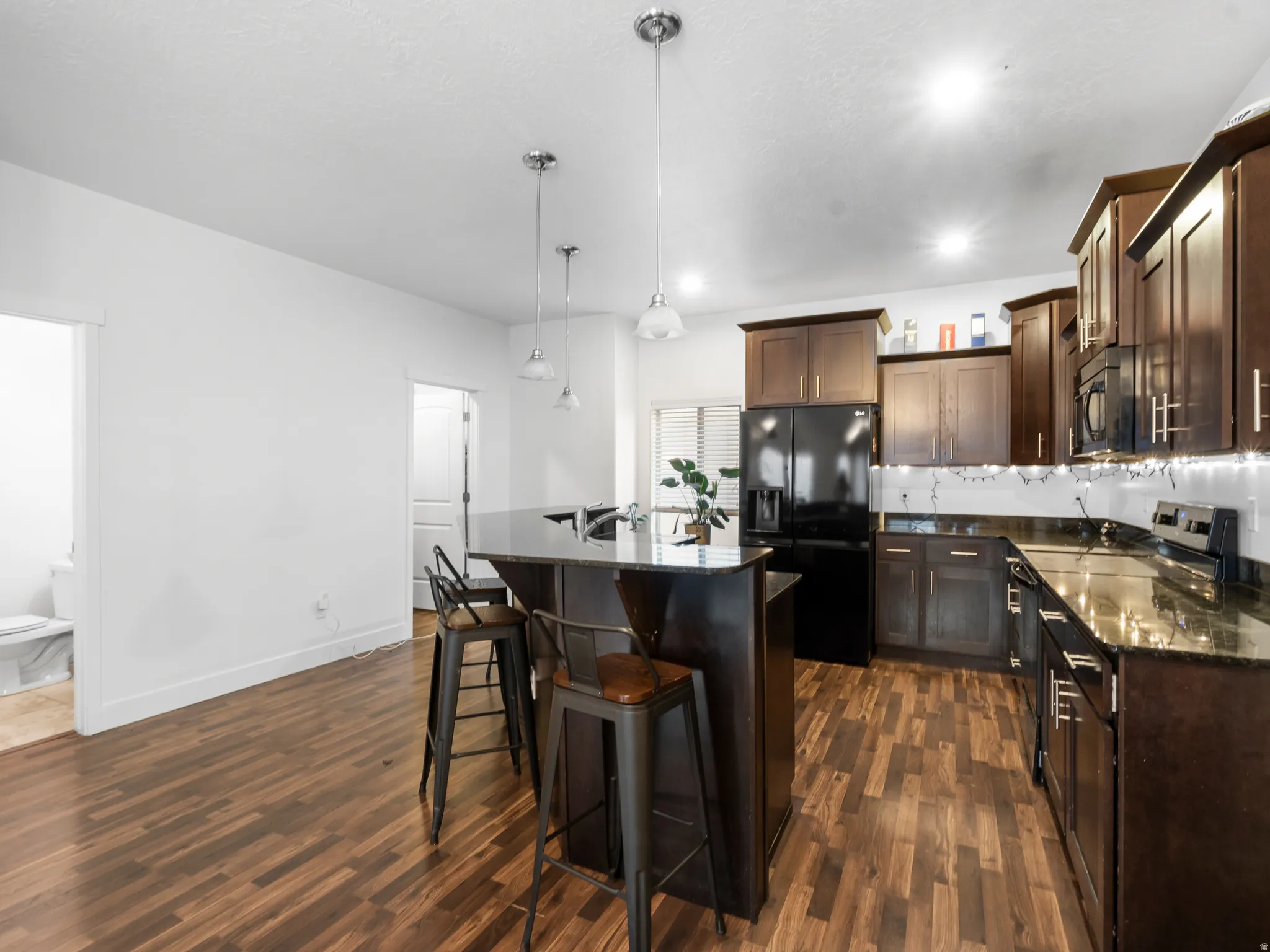 Kitchen with an island with sink, black appliances, a breakfast bar area, and dark stone countertops