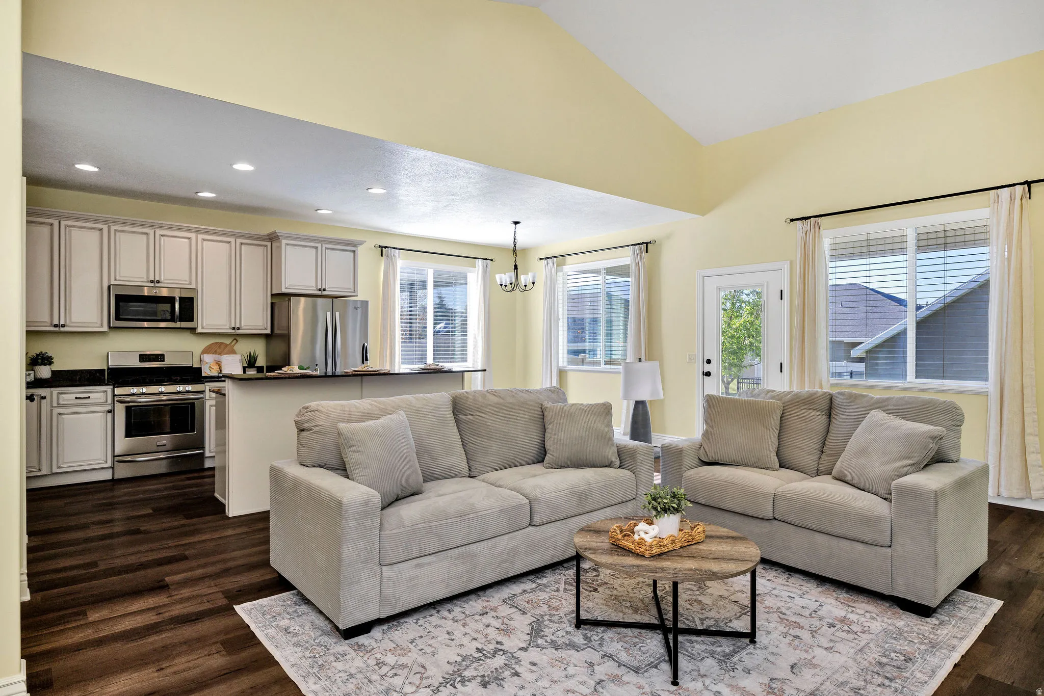 Living room with suspended lighting, healthy amount of natural light, dark wood-type flooring, and lofted ceiling