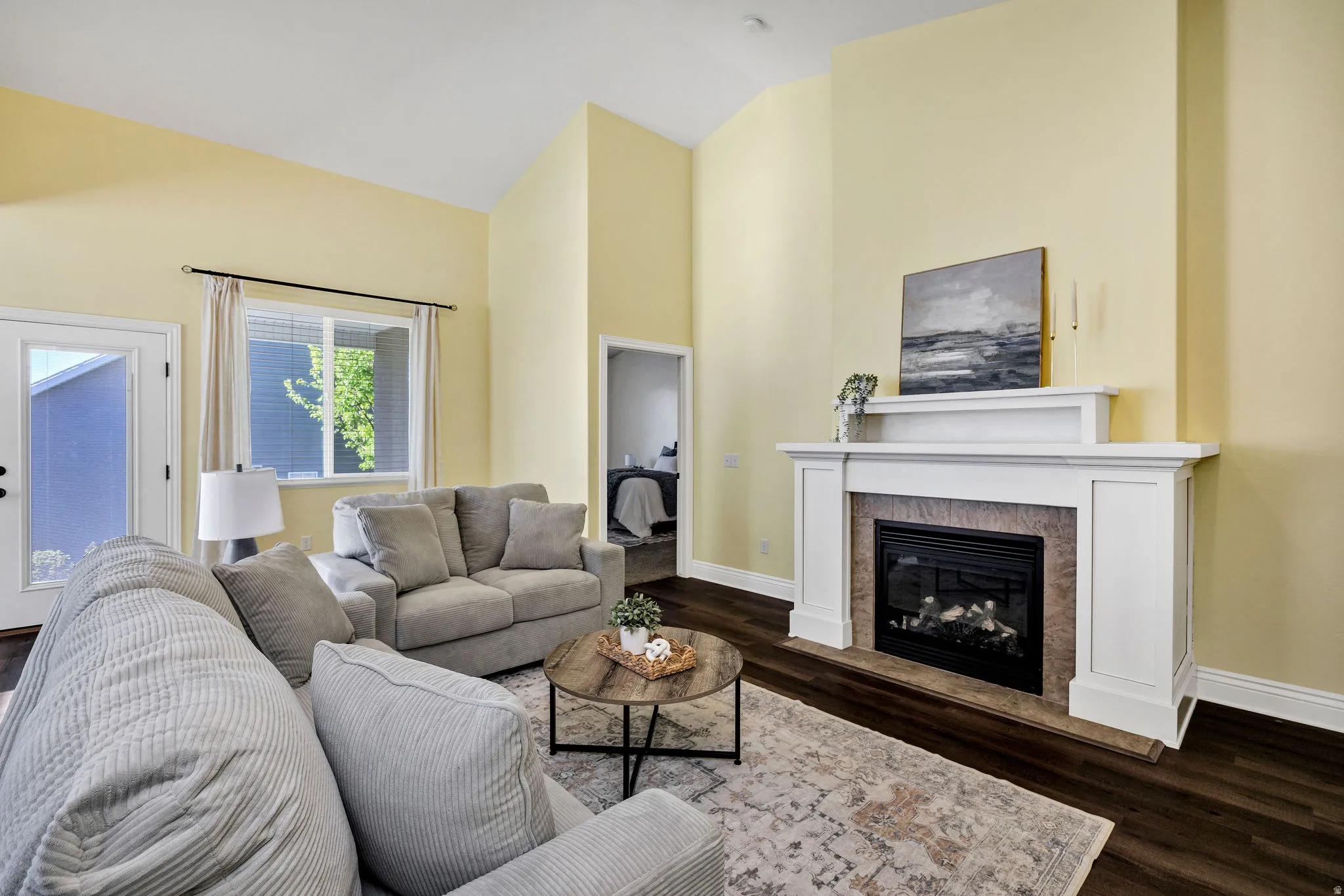 Living room with vaulted ceiling, dark wood-type flooring, and a tile fireplace