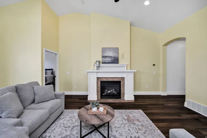 Living area with arched walkways, vaulted ceiling, dark wood-style floors, and a glass covered fireplace