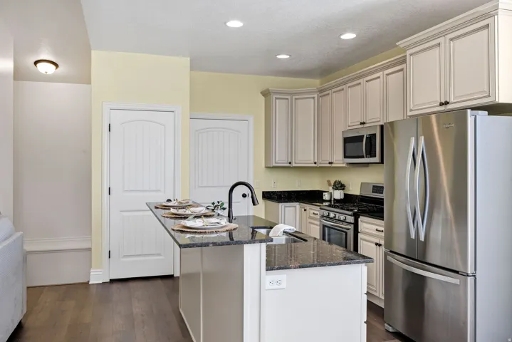 Kitchen with stainless steel appliances, dark stone countertops, an island with sink, dark wood-style floors, and recessed lighting
