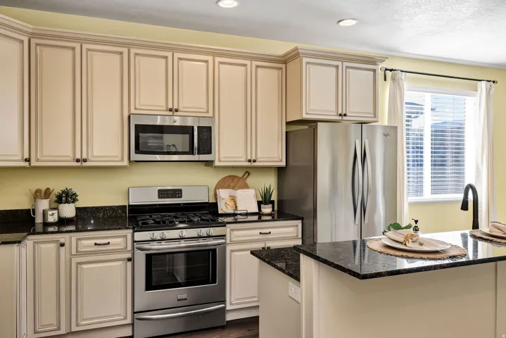 Kitchen featuring dark stone countertops, stainless steel appliances, cream cabinets, recessed lighting