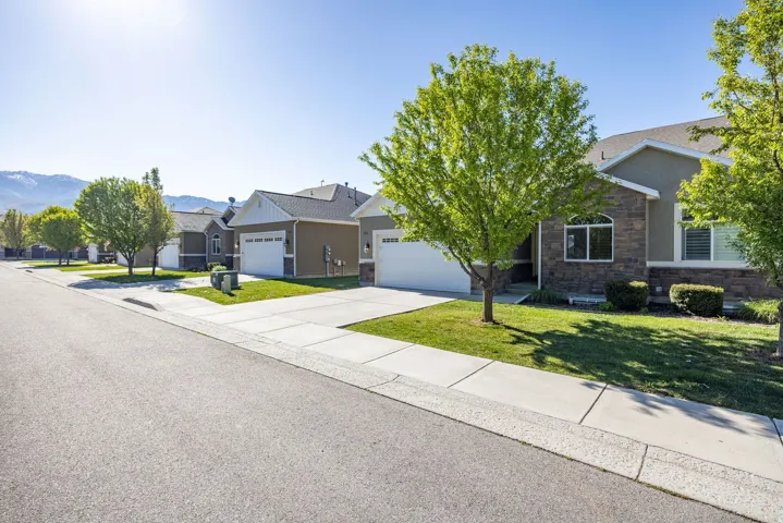 View of front of house featuring driveway, stone siding, an attached garage, a front lawn, and stucco siding