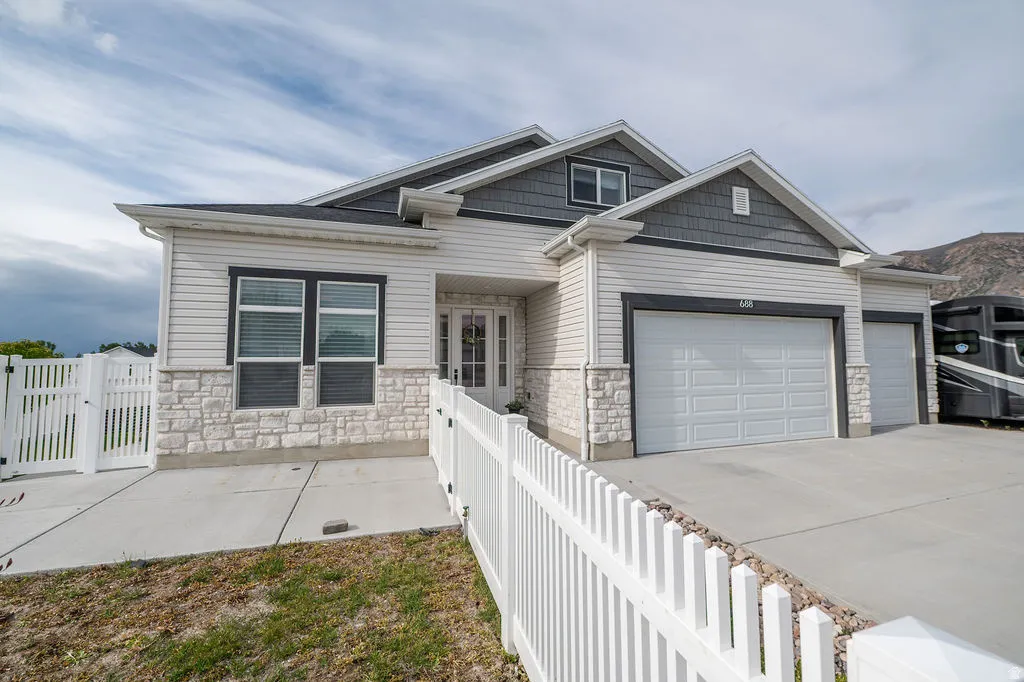 Craftsman house featuring driveway, an attached garage, stone siding, and a gate