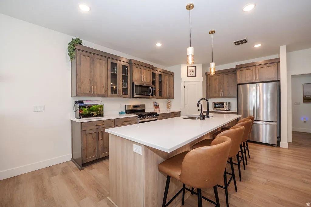 Kitchen with a breakfast bar area, stainless steel appliances, glass insert cabinets, a kitchen island with sink, and light wood-style floors