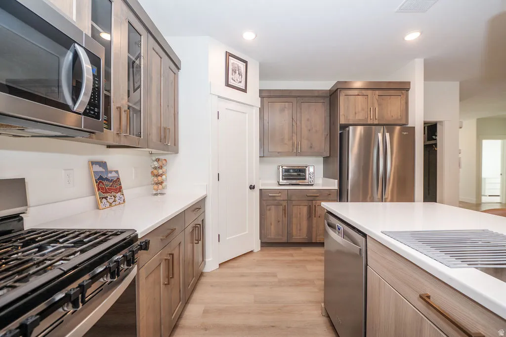 Kitchen with glass fronted cabinets, stainless steel appliances, light wood-type flooring, recessed lighting, and wood finish cabinets
