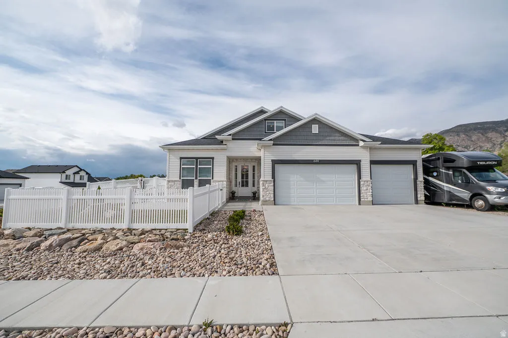 View of front of home with a fenced front yard, a garage, driveway, and stone siding