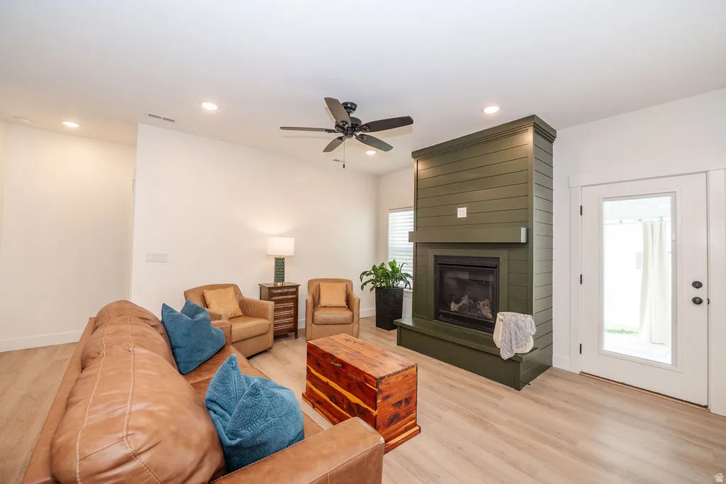 Living area featuring light wood-style floors, ceiling fan, a large fireplace, and recessed lighting