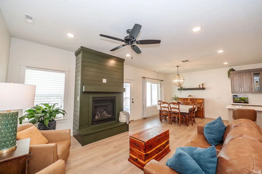Living room with light wood-style floors, a ceiling fan, a large fireplace, and suspended lighting