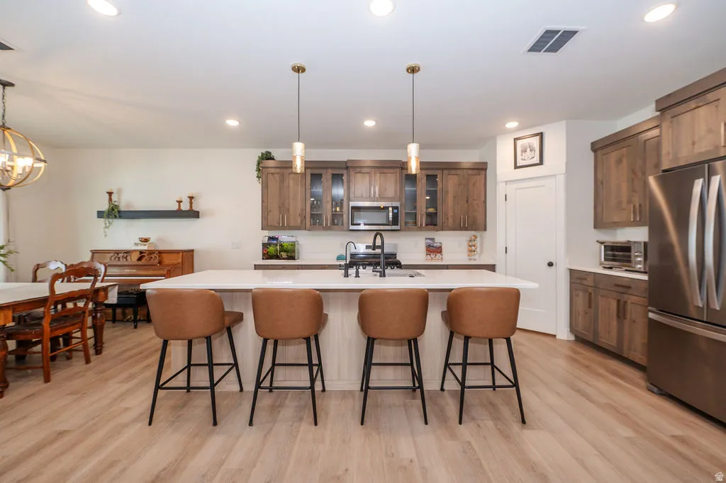Kitchen featuring glass insert cabinets, stainless steel appliances, a breakfast bar, and light wood finished floors