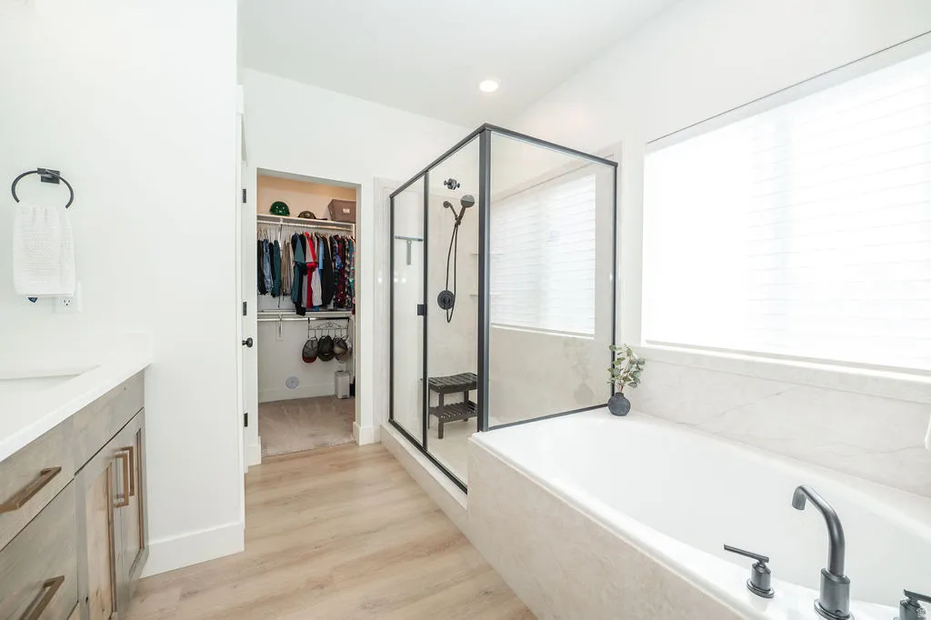 Full bath featuring a stall shower, vanity, a bath, a spacious closet, and light wood-style floors