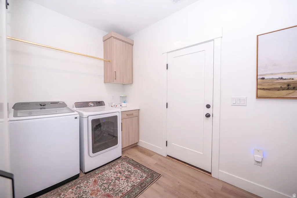 Laundry room with light wood finished floors, washing machine and clothes dryer, and cabinet space