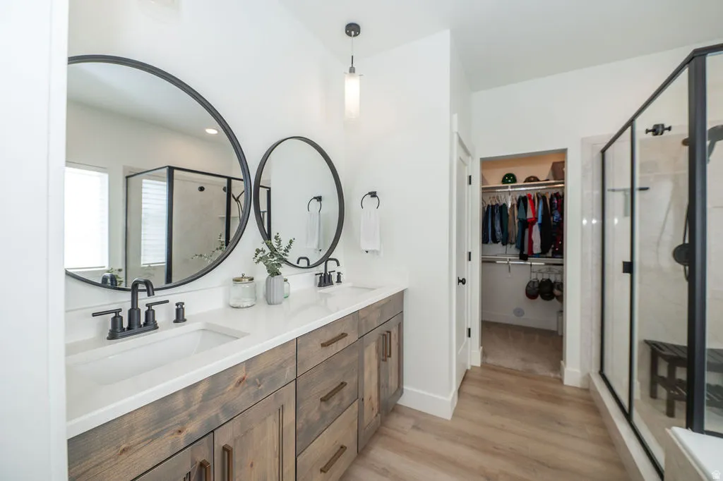 Full bathroom with a shower stall, double vanity, light wood-style flooring, and a walk in closet