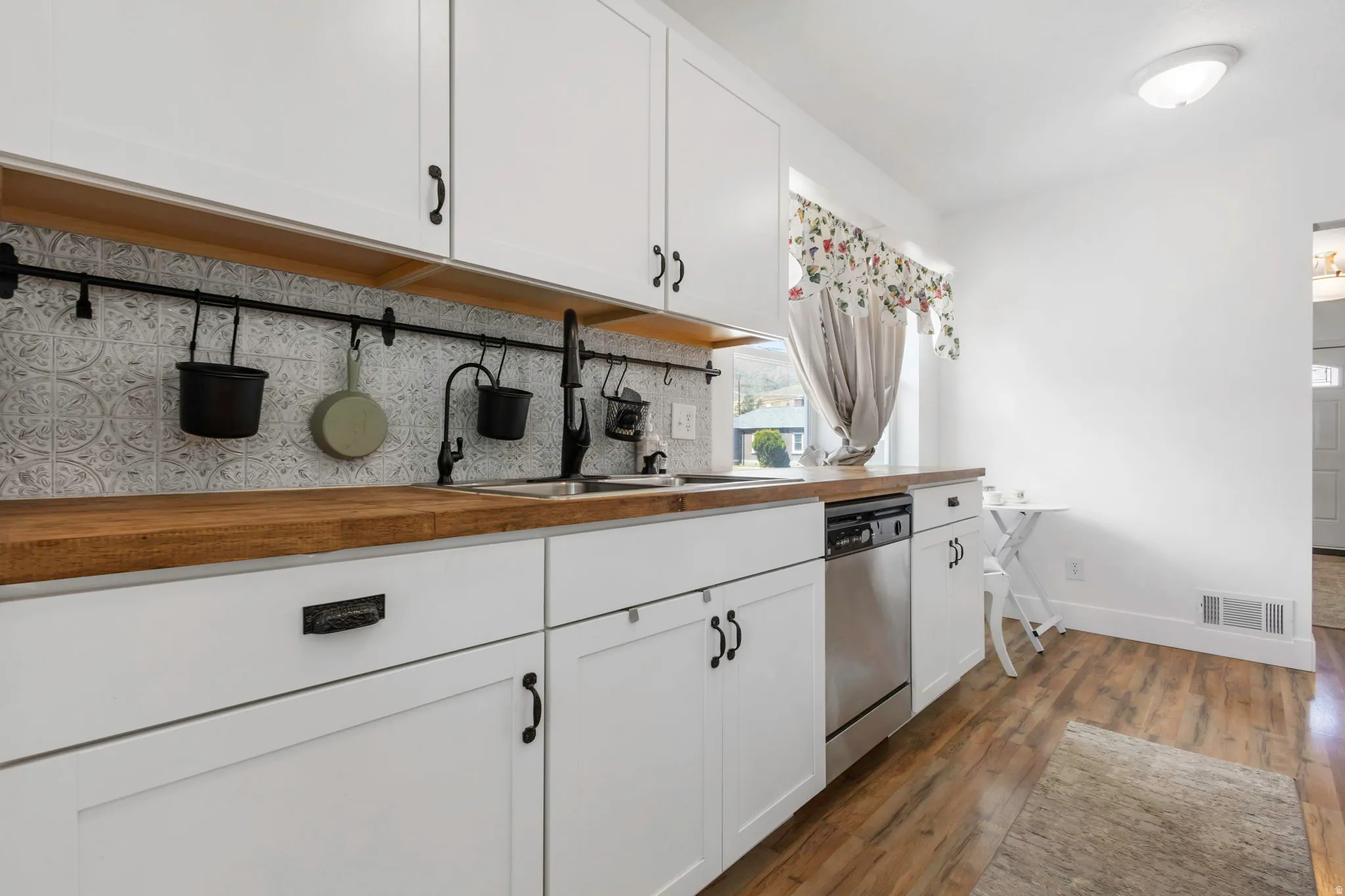 Kitchen with butcher block countertops, white cabinetry, dark wood-style flooring, dishwasher, and tasteful backsplash