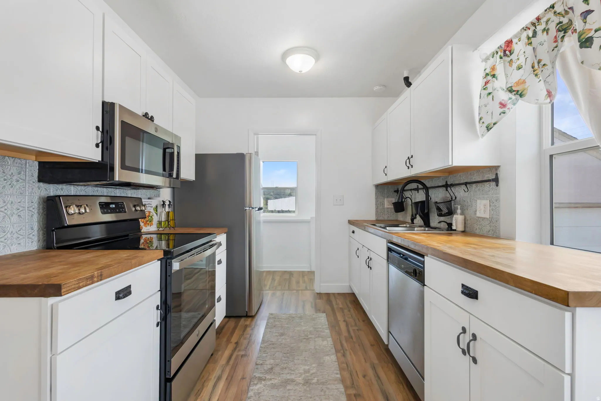 Kitchen featuring butcher block countertops, stainless steel appliances, white cabinets, and backsplash