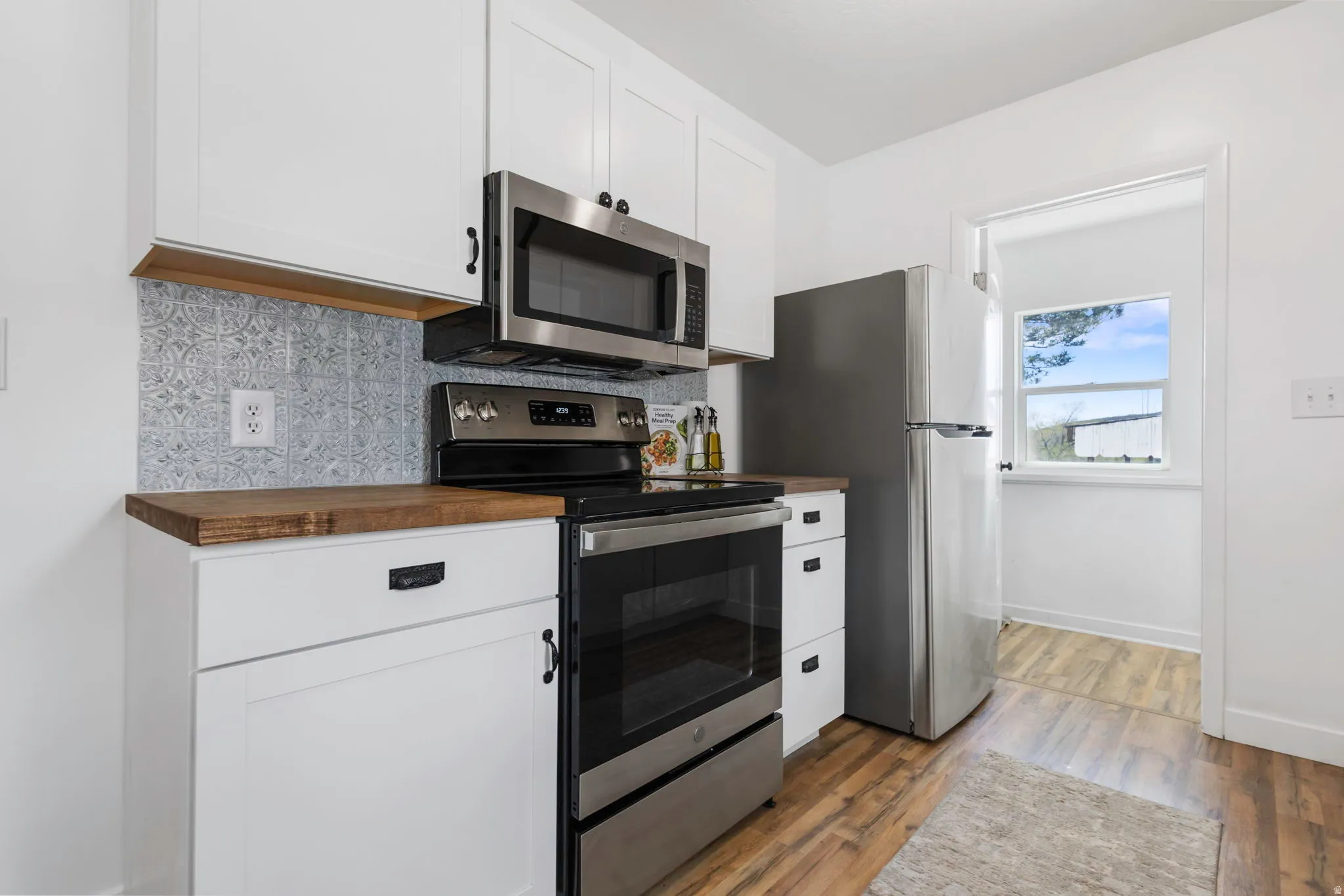 Kitchen with wooden counters, stainless steel appliances, tasteful backsplash, light wood-type flooring, and white cabinetry