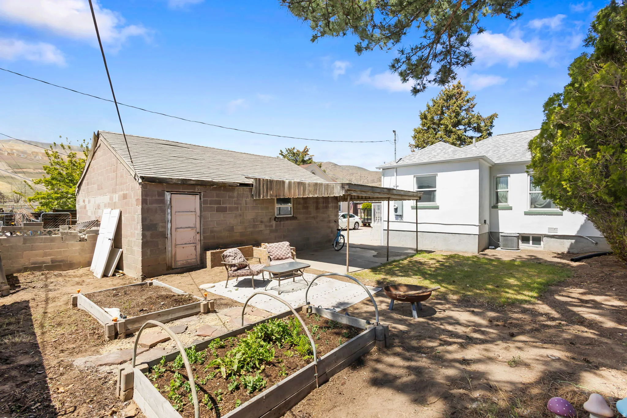 Rear view of house featuring a garden, a patio area, roof with shingles, and an outdoor fire pit