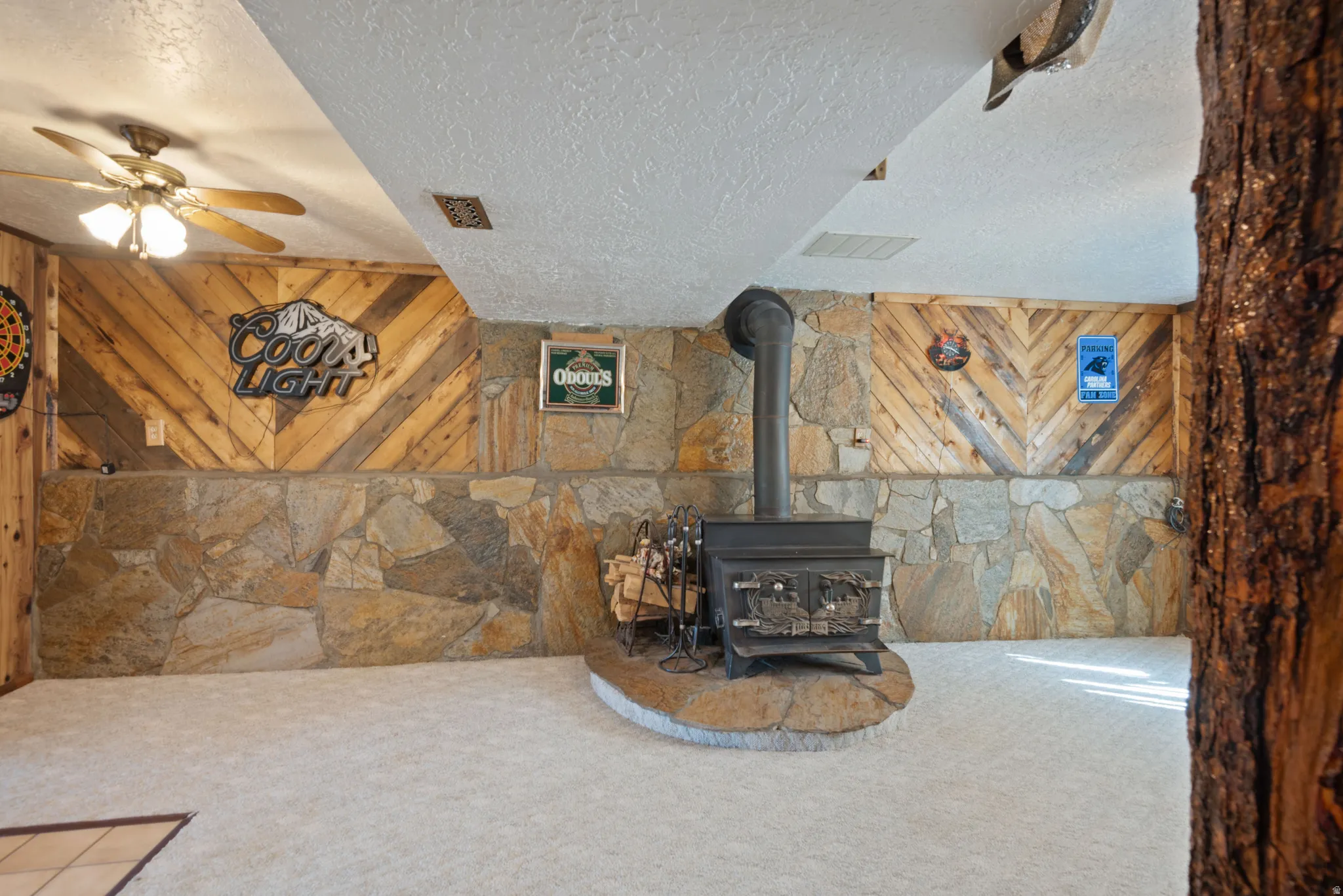 Unfurnished living room featuring a textured ceiling, a wood stove, carpet floors, ceiling fan, and wood walls