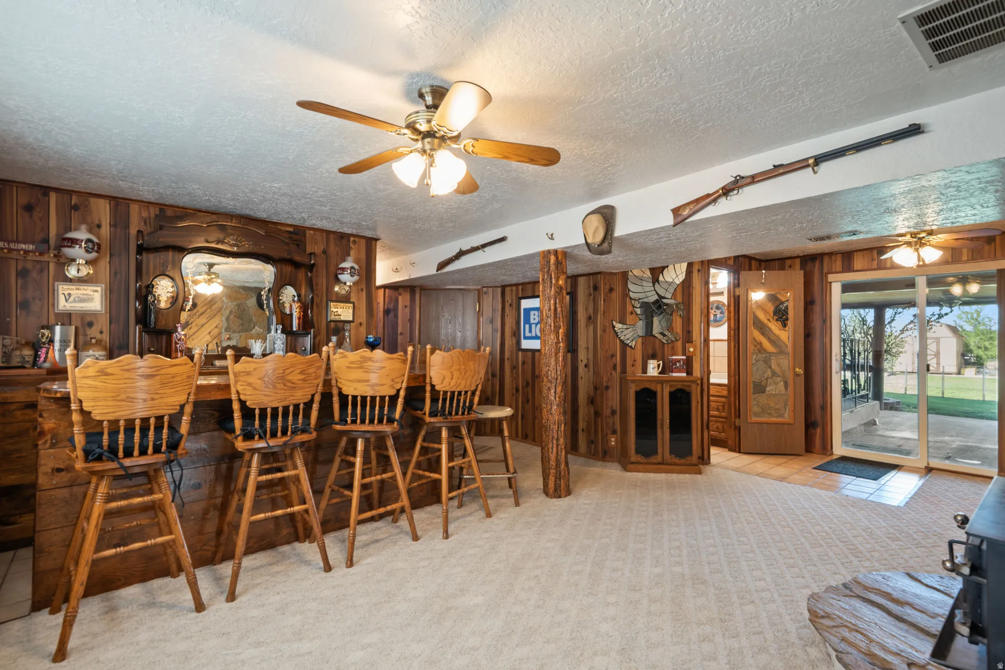 Dining area with ceiling fan, light colored carpet, a textured ceiling, wooden walls, and a dry bar