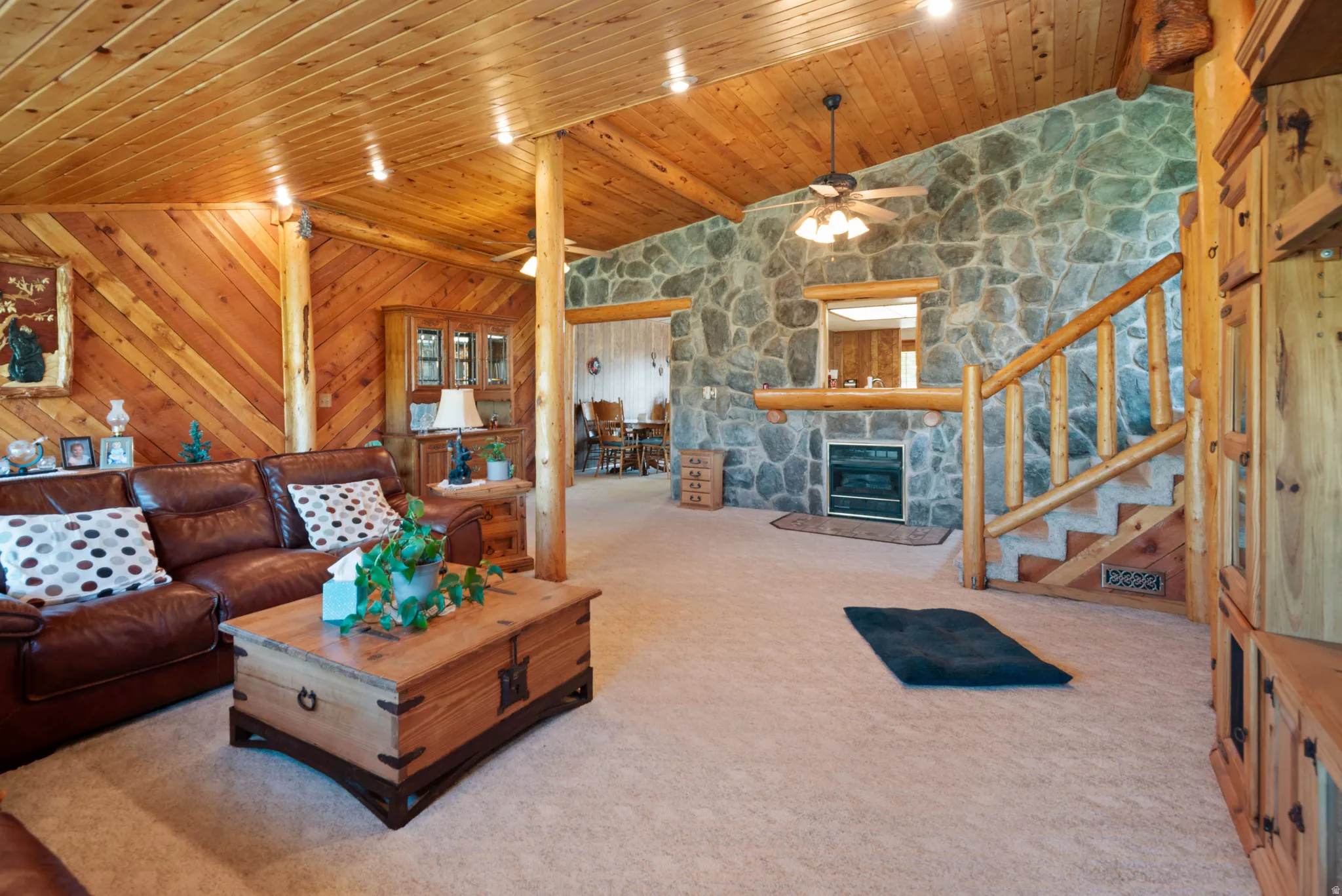 Carpeted living area with vaulted ceiling with beams, wood ceiling, a fireplace, and ceiling fan