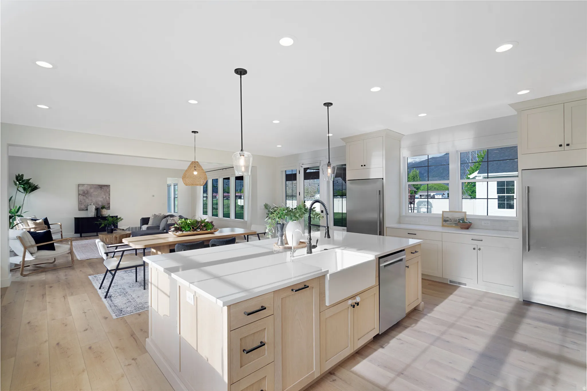 Kitchen with stainless steel appliances, open floor plan, a center island with sink, light wood finished floors, and hanging light fixtures