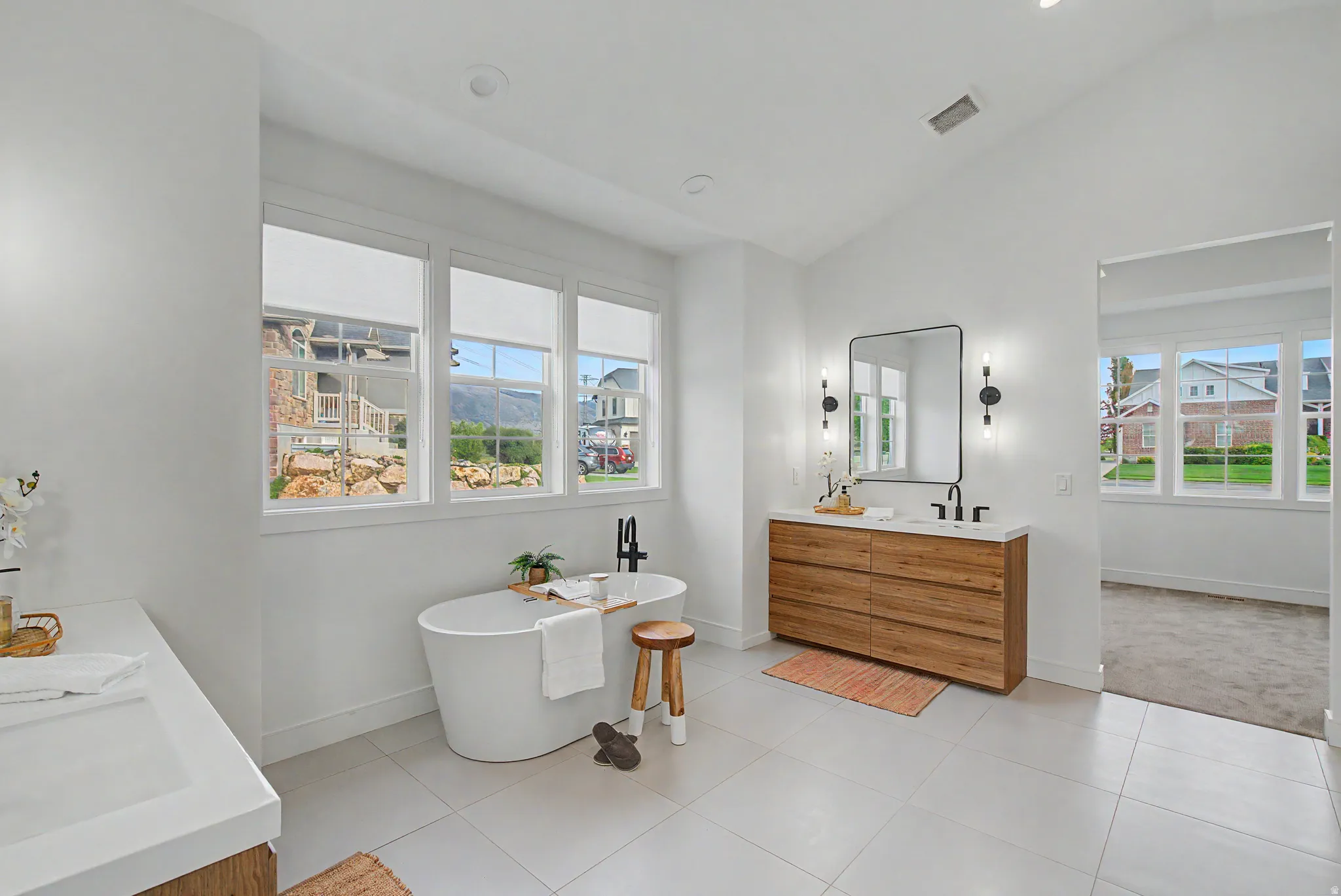 Bathroom featuring double vanity, lofted ceiling, a freestanding tub, recessed lighting, and light tile patterned floors