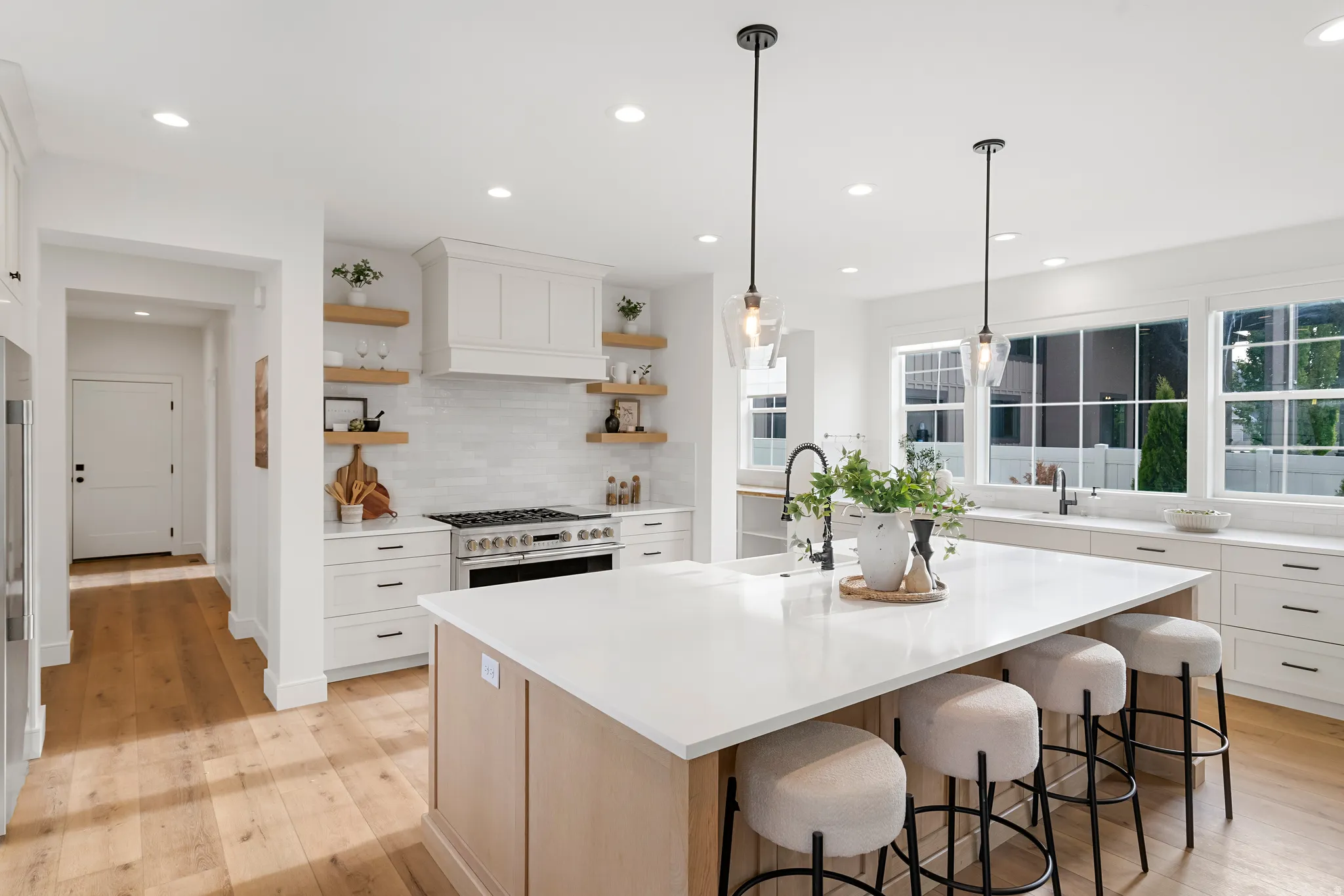 Two tone kitchen featuring an island with sink, decorative light fixtures, light wood finished floors, open shelves, and a breakfast bar