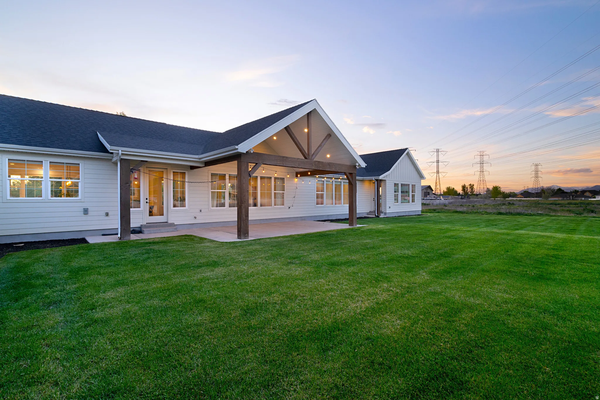 Back of property at dusk featuring a patio area, a lawn, and a shingled roof