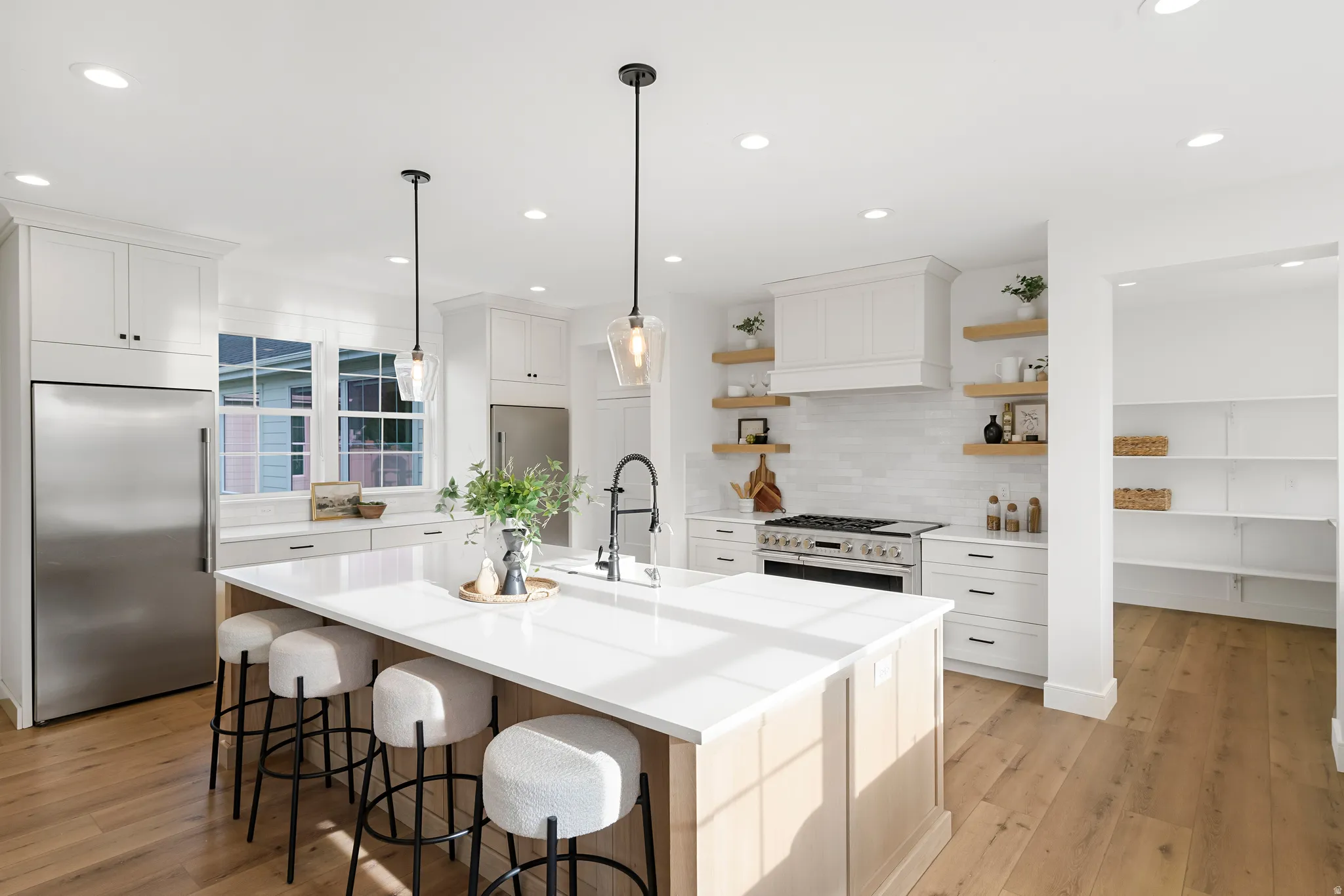 Kitchen featuring high quality appliances, light wood-style flooring, white cabinets, and a kitchen island with sink