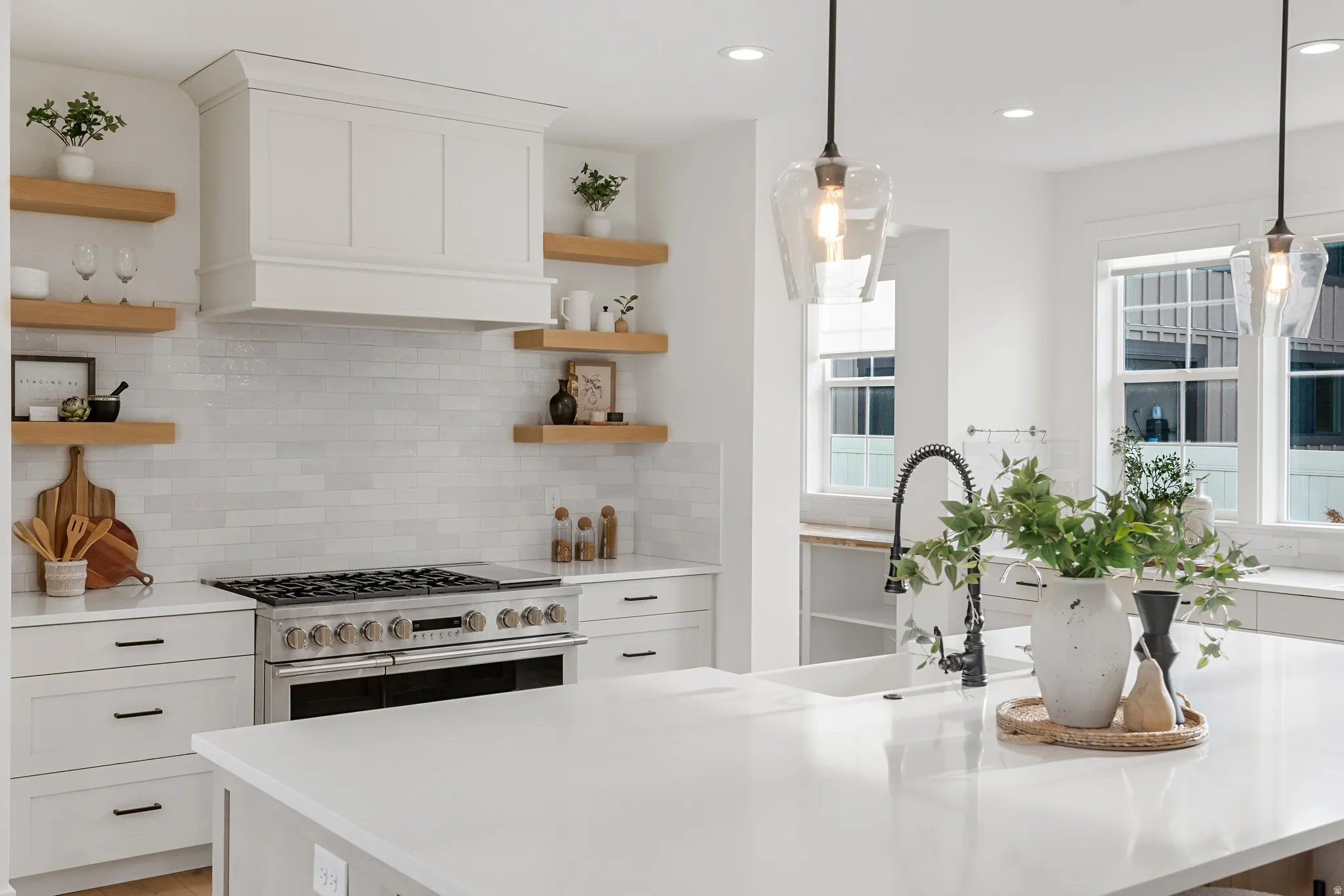 Kitchen with open shelves, white cabinets, range with two ovens, and light stone counters