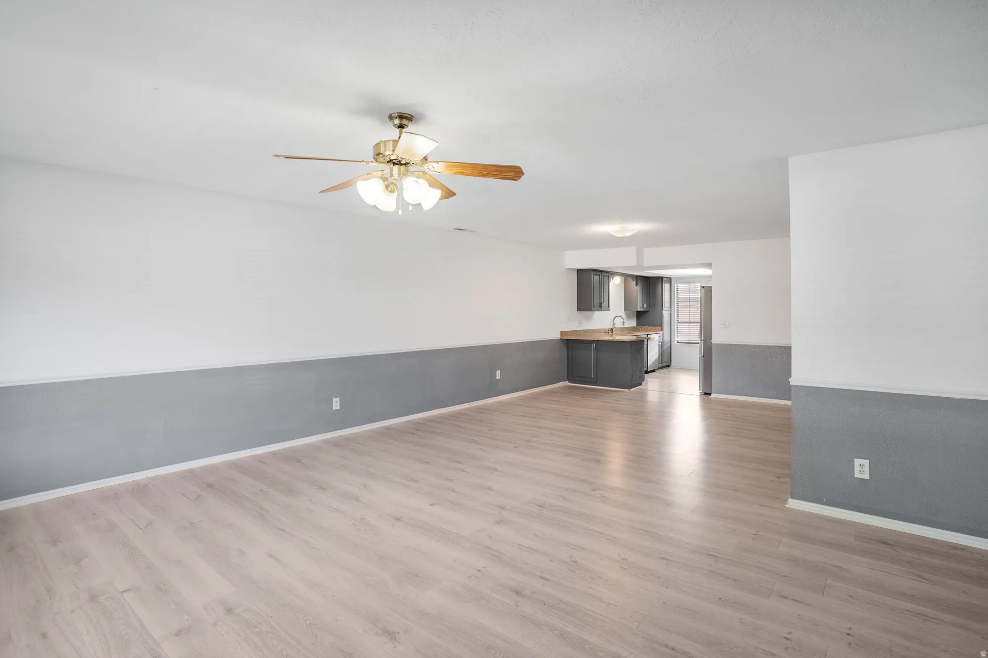 Unfurnished living room with ceiling fan, light wood-type flooring, and wainscoting