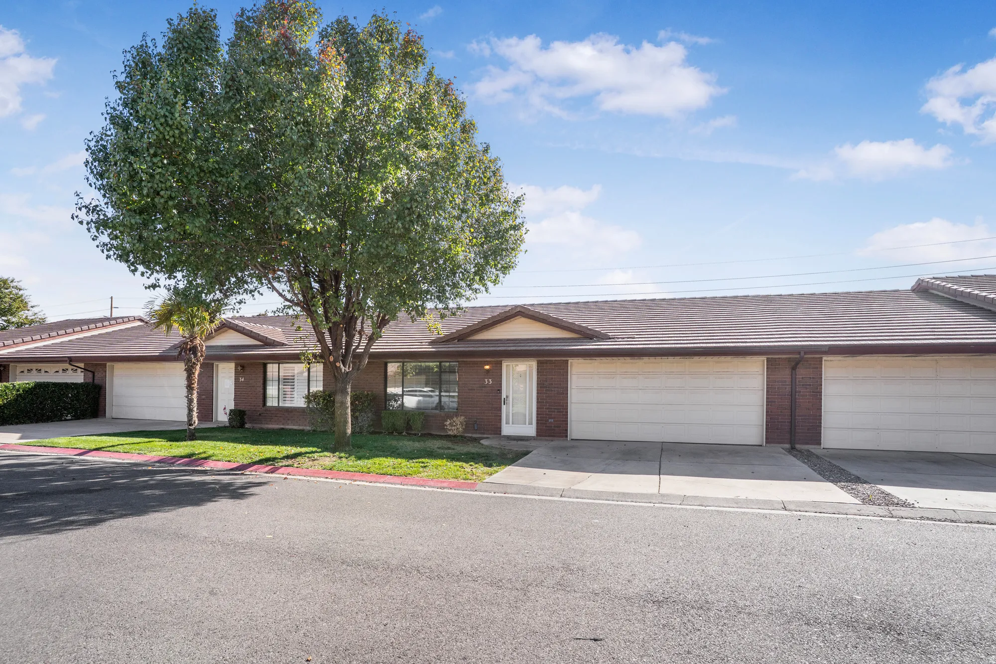 Ranch-style home featuring brick siding, driveway, a tile roof, a garage, and a front lawn