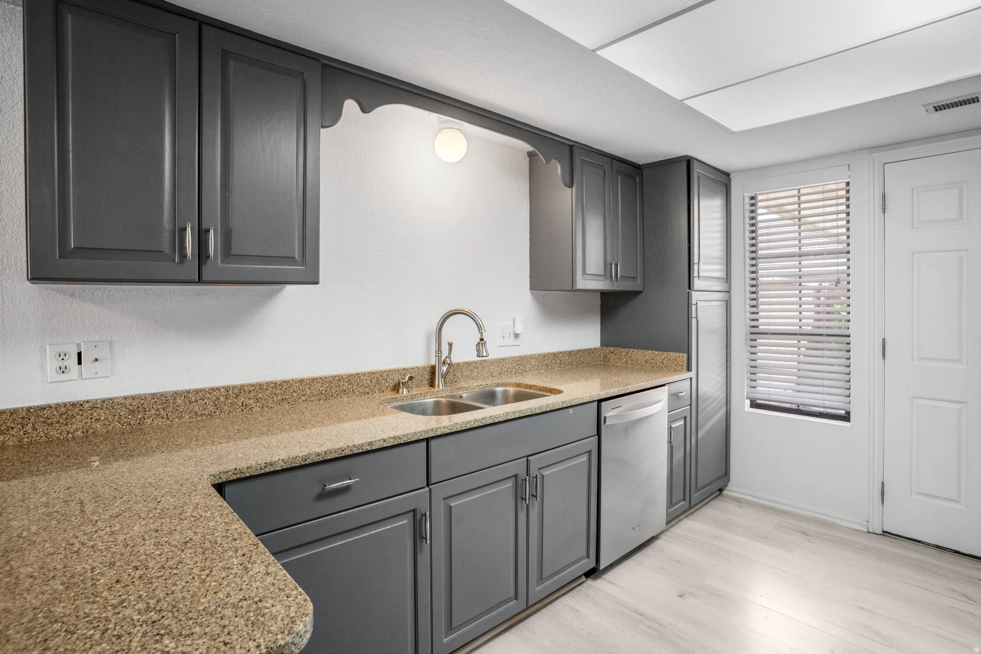 Kitchen featuring gray cabinets, light stone counters, light wood-type flooring, and stainless steel dishwasher