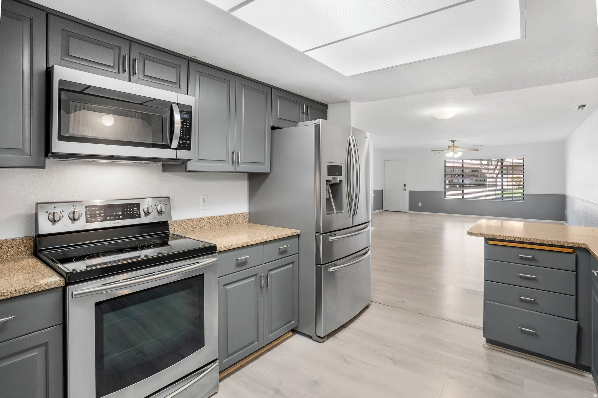 Kitchen featuring gray cabinets, stainless steel appliances, light wood-type flooring, light stone counters, and a wainscoted wall