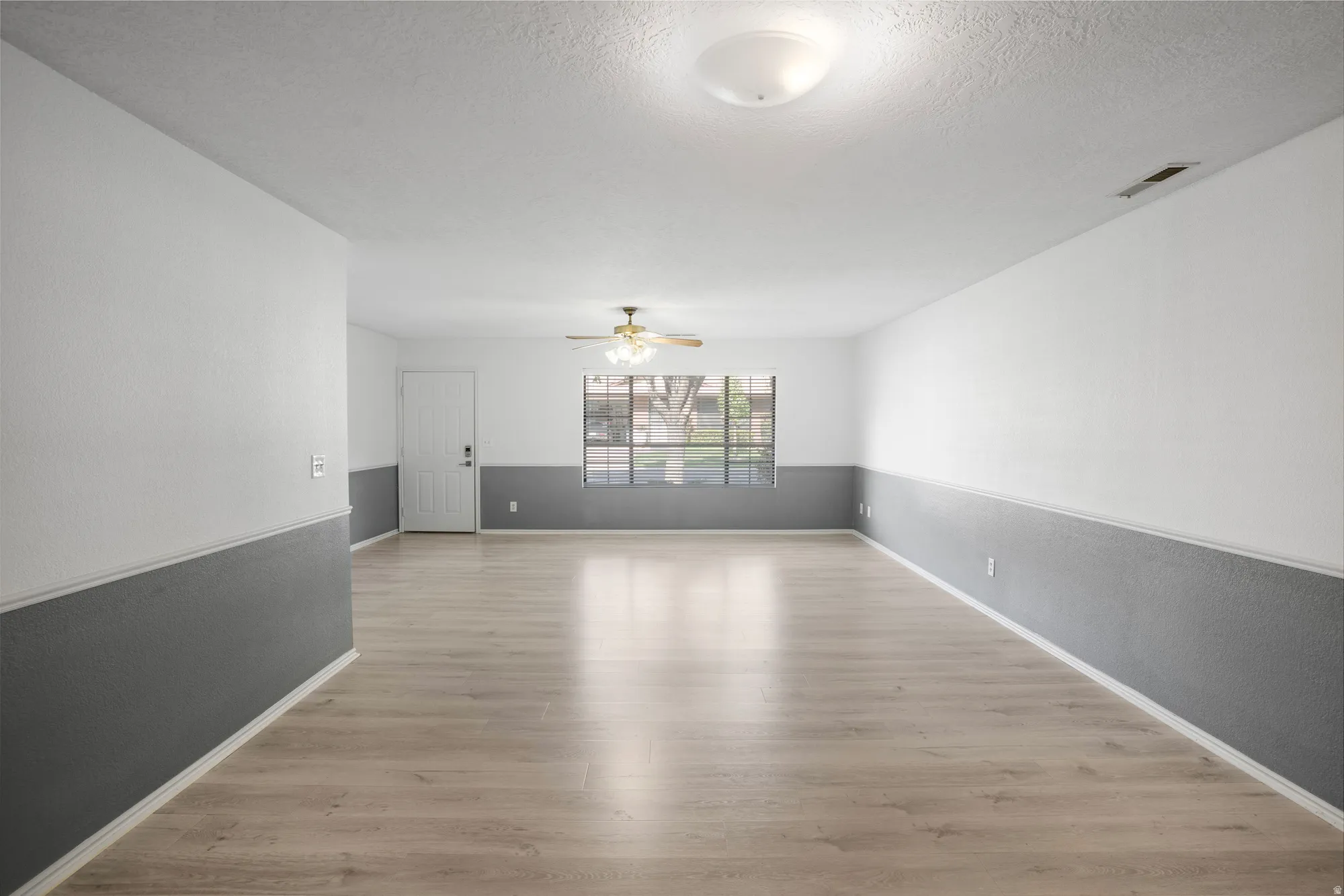 Empty room with light wood finished floors, a ceiling fan, a textured ceiling, and a textured wall