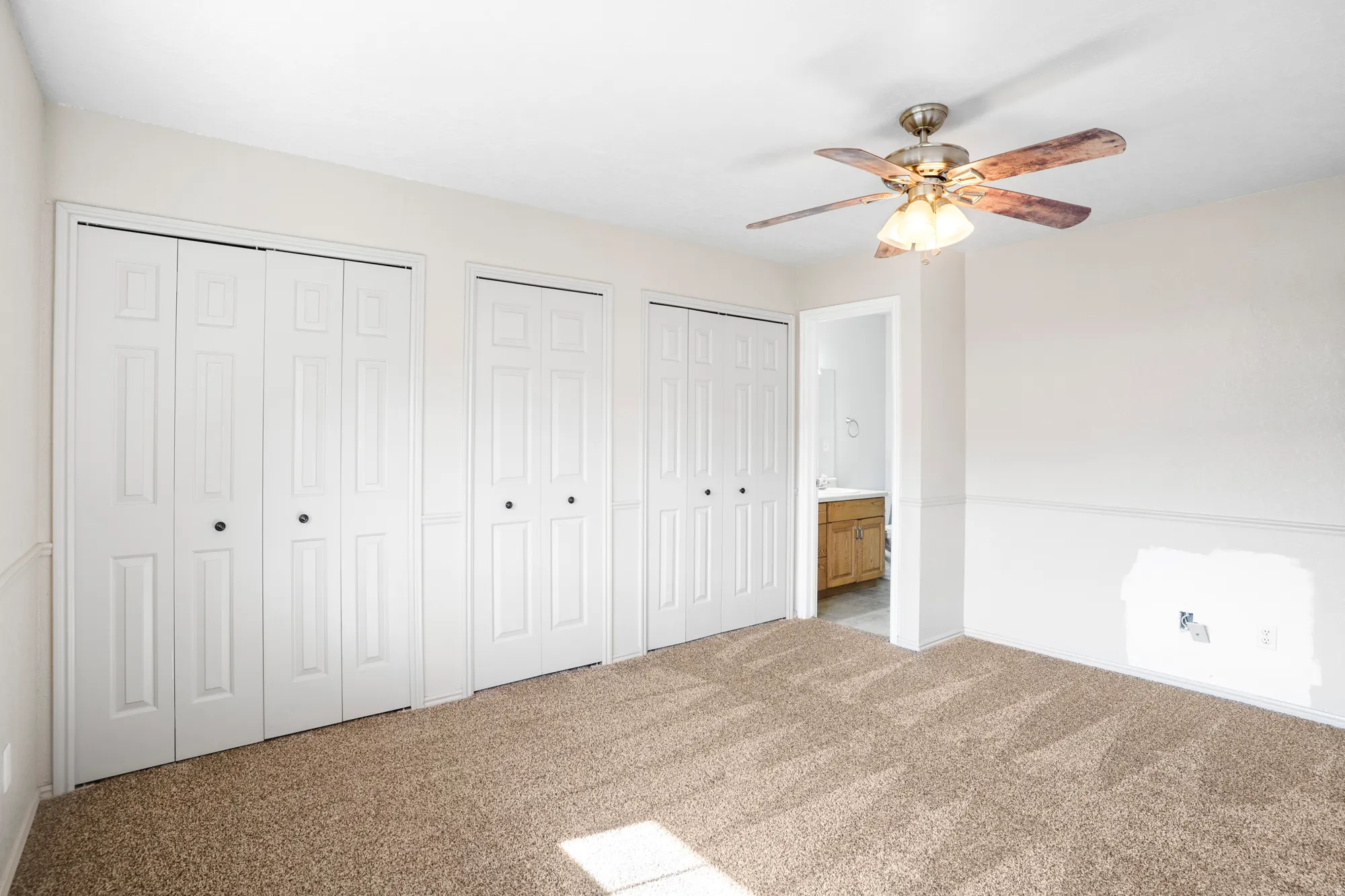 Unfurnished bedroom featuring multiple closets, connected bathroom, light colored carpet, and a ceiling fan