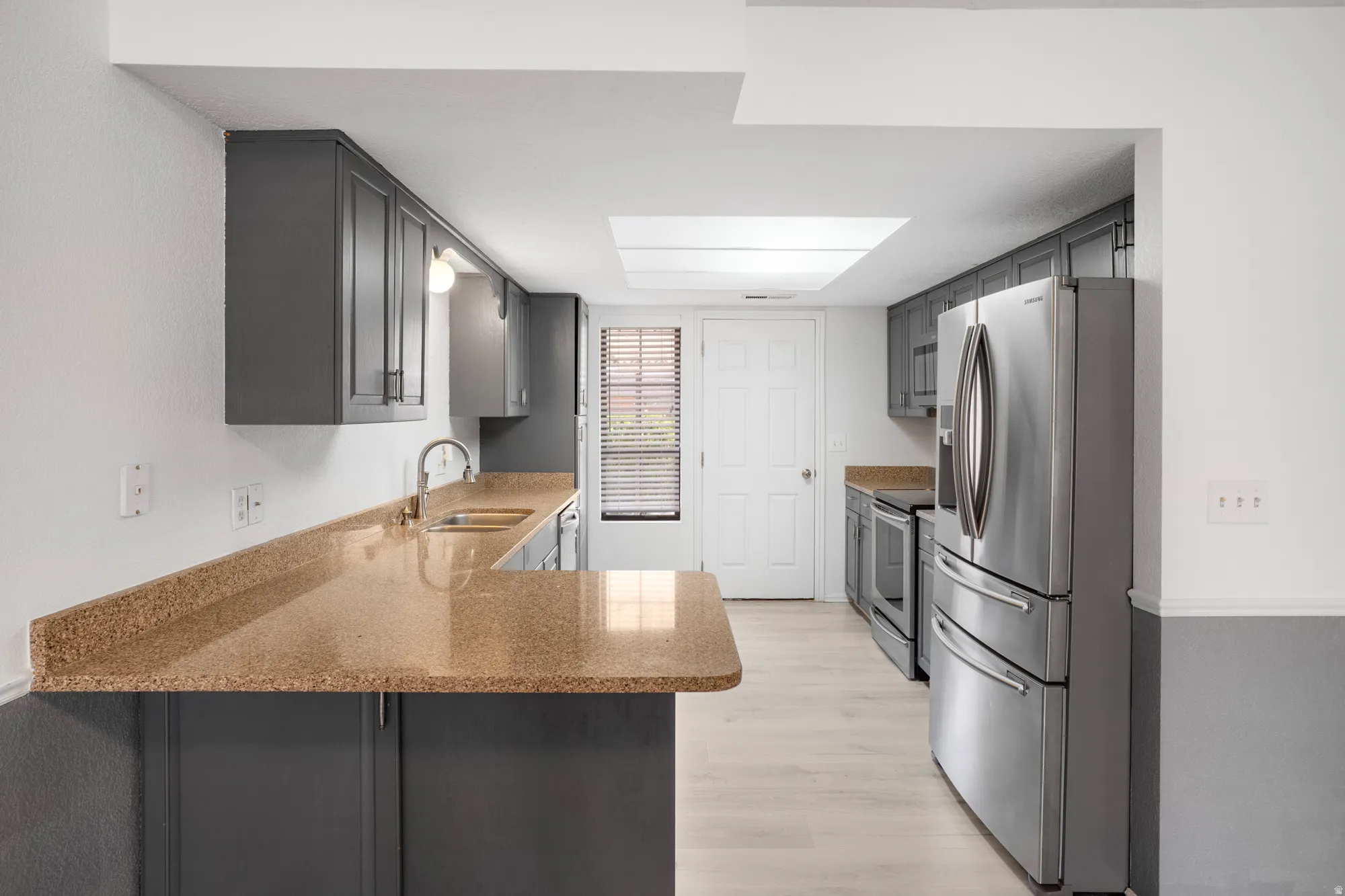 Kitchen with stainless steel appliances, light wood finished floors, light stone countertops, and gray cabinetry