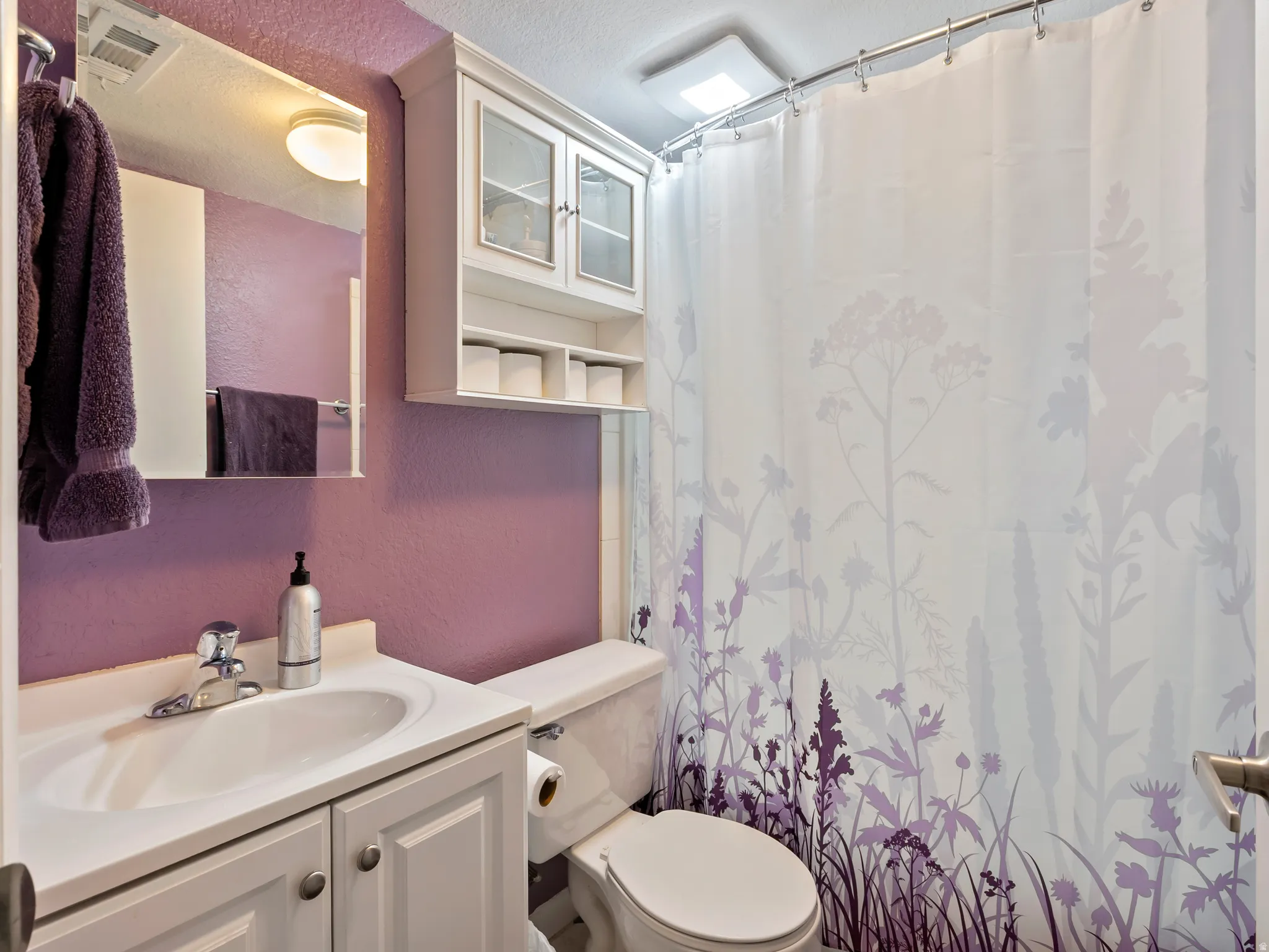 Full bathroom featuring a textured wall, vanity, curtained shower, and a textured ceiling