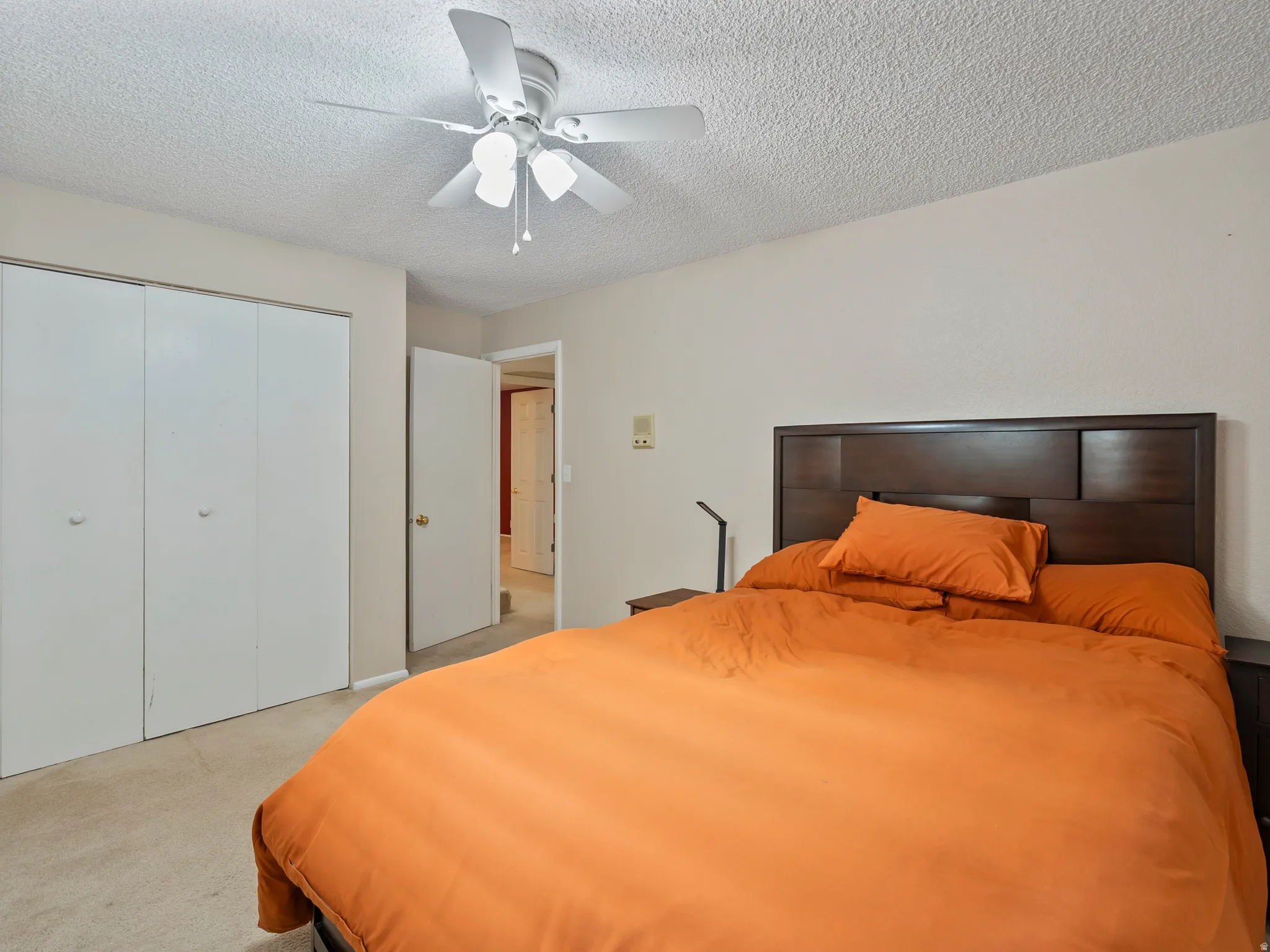 Bedroom featuring a textured ceiling, a closet, light carpet, and ceiling fan