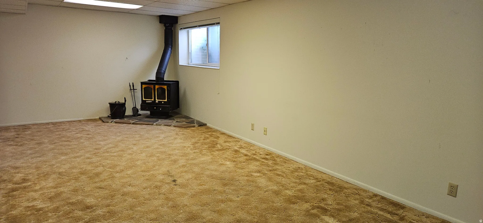 Unfurnished living room featuring a wood stove, carpet flooring, and a drop ceiling
