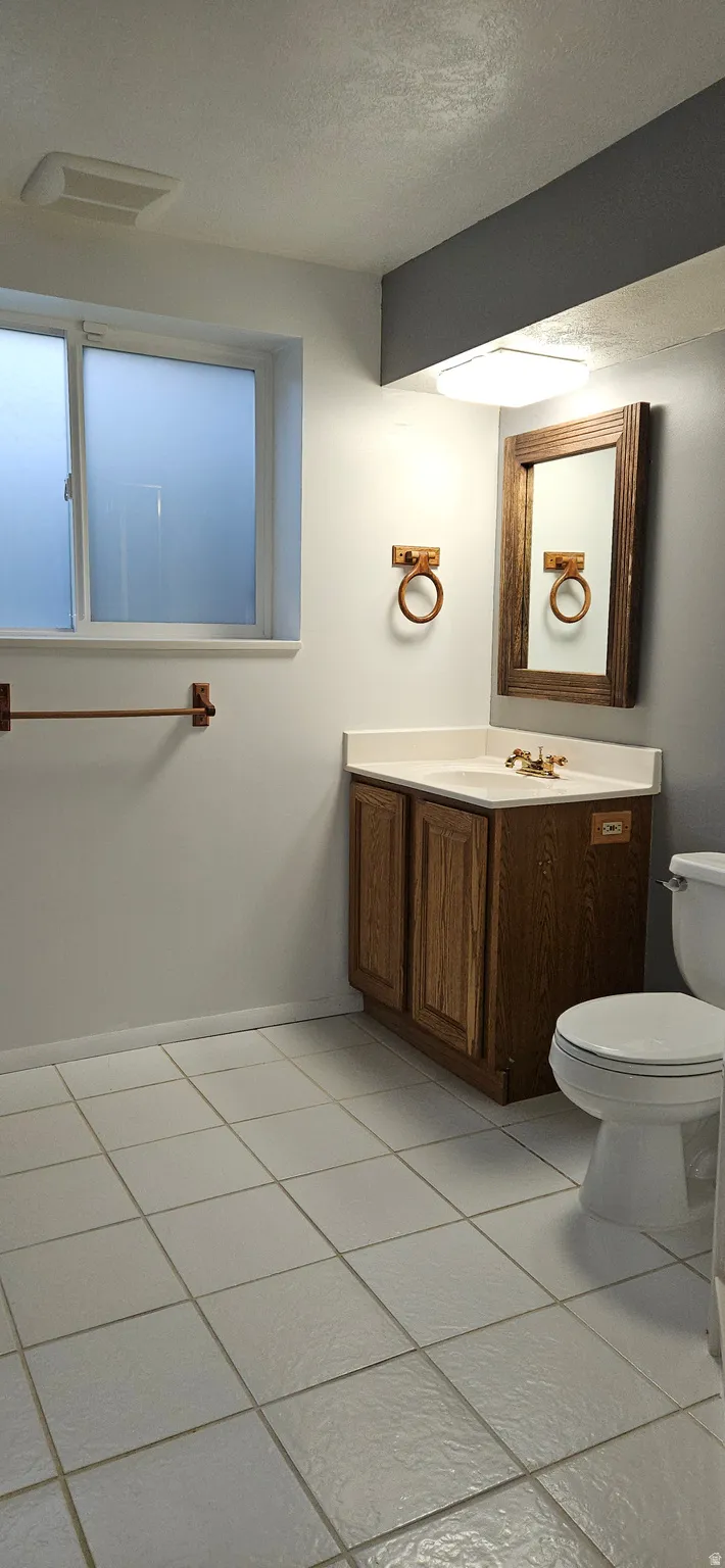 Half bath with vanity, a textured ceiling, and light tile patterned floors