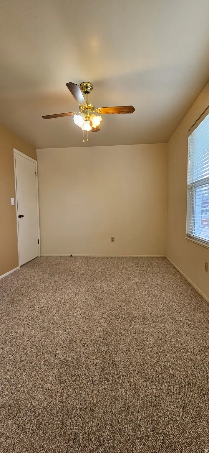 Carpeted empty room with a ceiling fan and baseboards