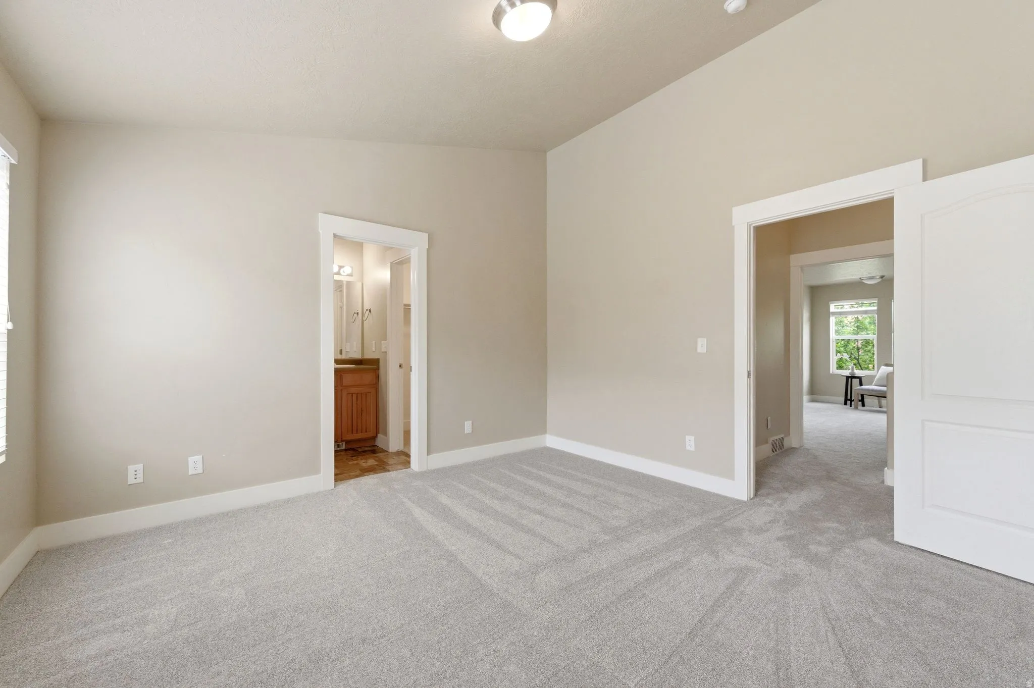 Unfurnished bedroom with light carpet, ensuite bathroom, and vaulted ceiling