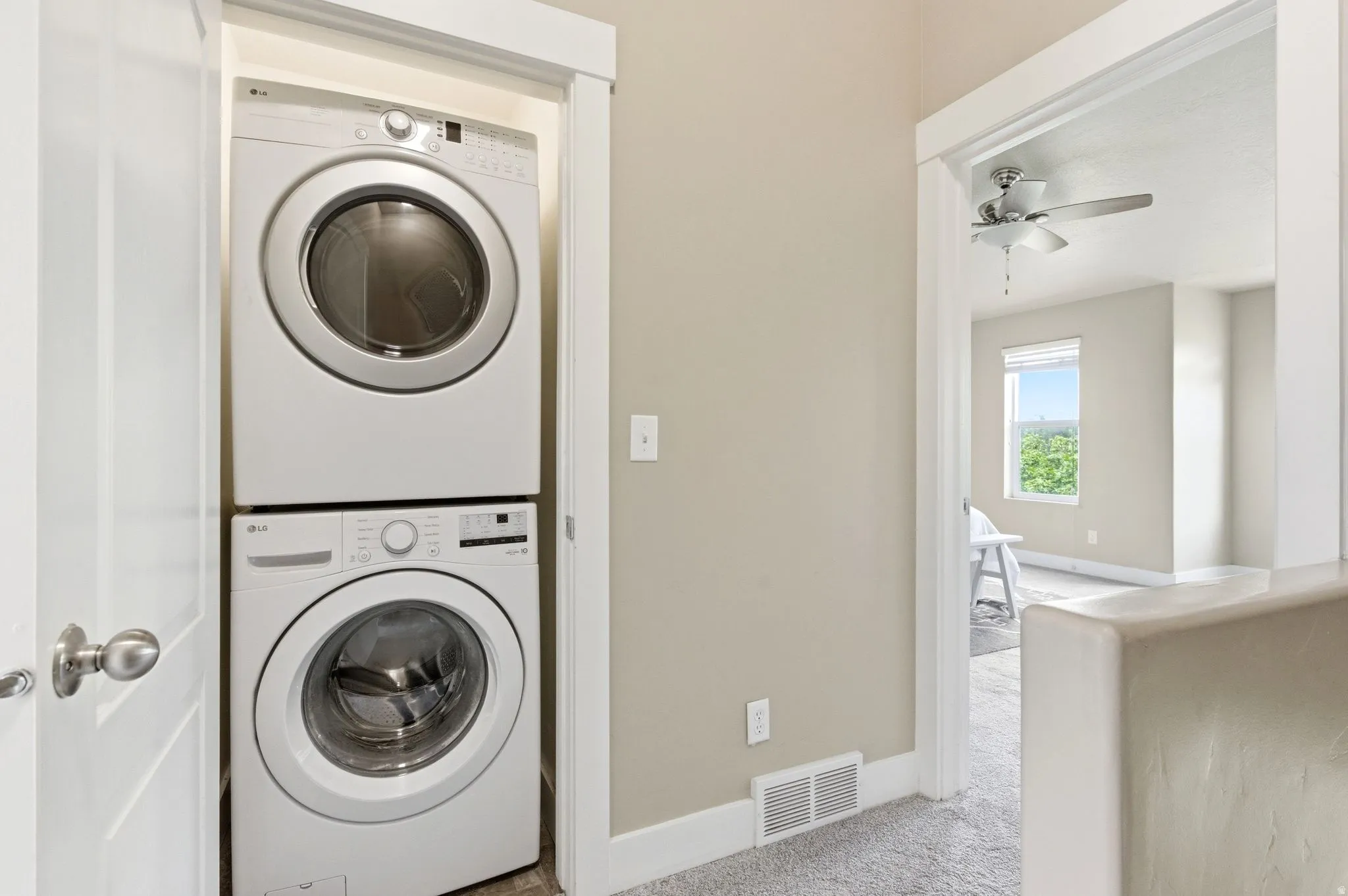 Laundry area featuring stacked washer and dryer, light colored carpet, and ceiling fan