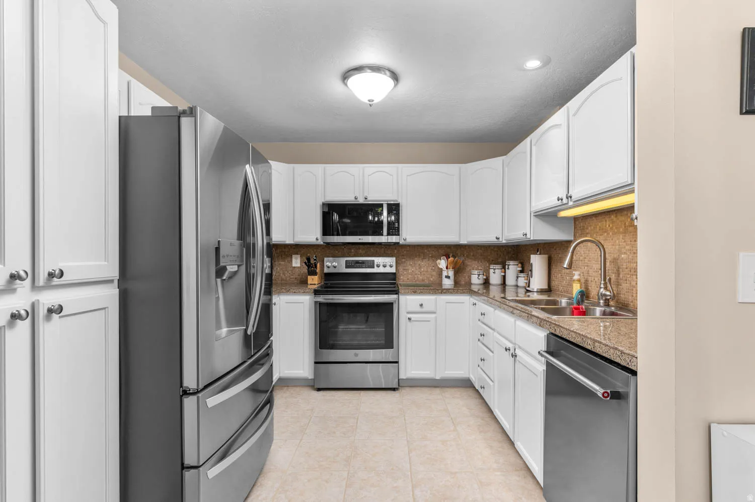 Kitchen featuring stainless steel appliances, white cabinets, decorative backsplash, light tile patterned flooring, and light countertops