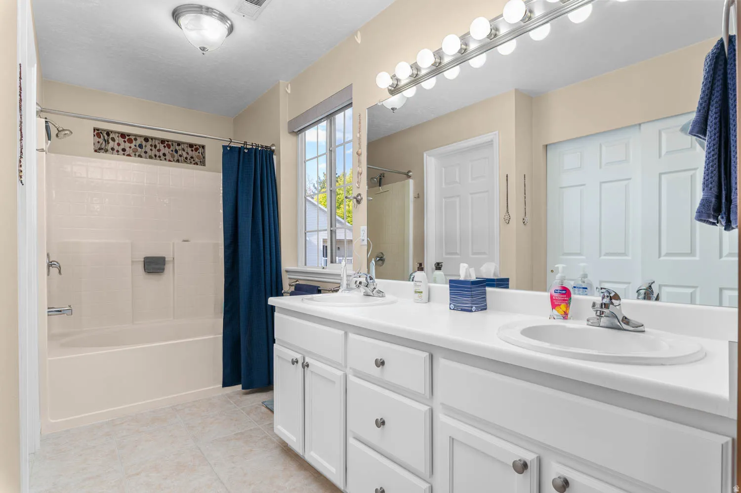 Bathroom with double vanity, shower / bath combo with shower curtain, and light tile patterned floors