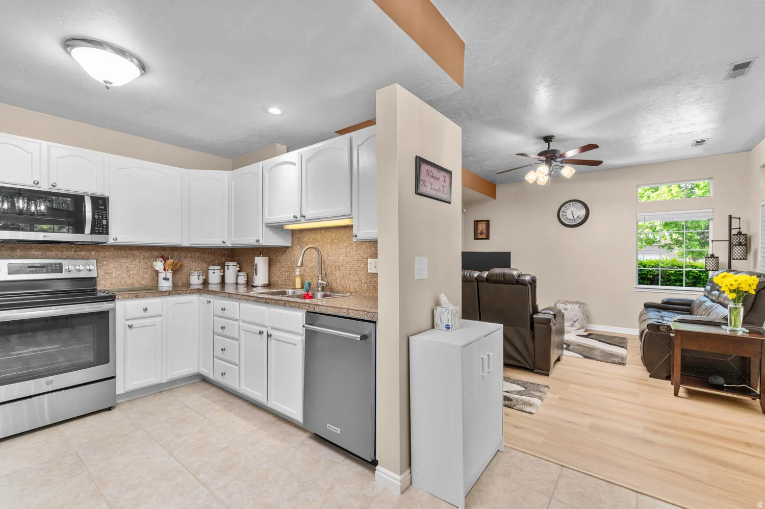 Kitchen with open floor plan, stainless steel appliances, light tile patterned floors, tasteful backsplash, and white cabinets