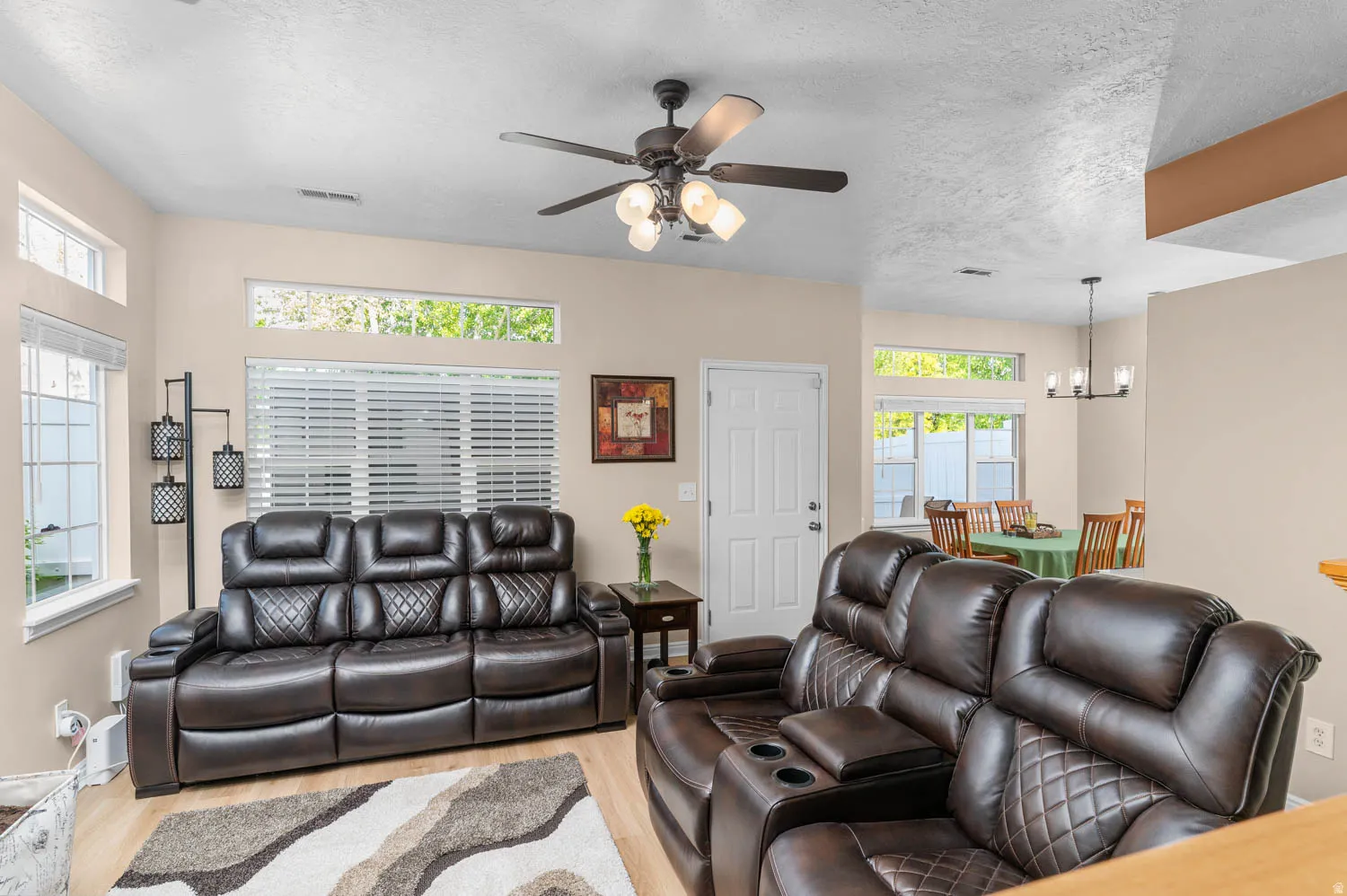 Living area with light wood finished floors, suspended lighting, a ceiling fan, and a textured ceiling