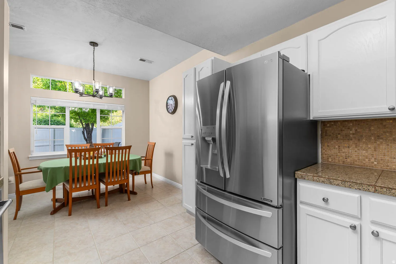 Kitchen featuring stainless steel fridge with ice dispenser, white cabinetry, tile counters, a chandelier, and decorative backsplash